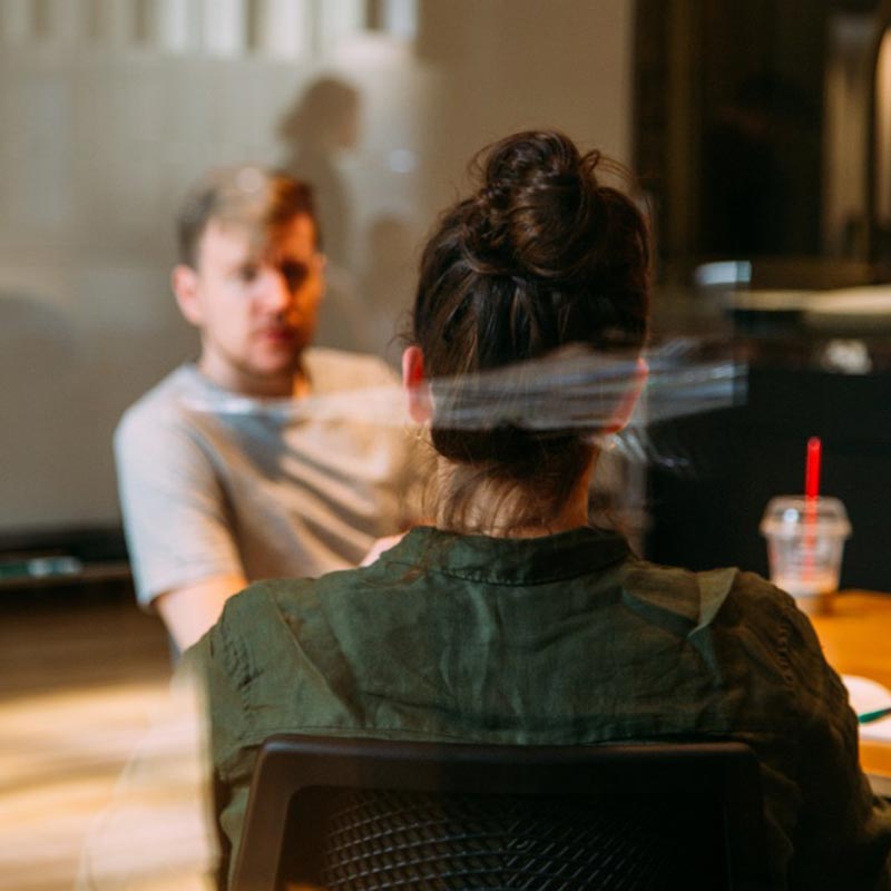 A man and a woman are visible through a glass window. Photo: Unsplash